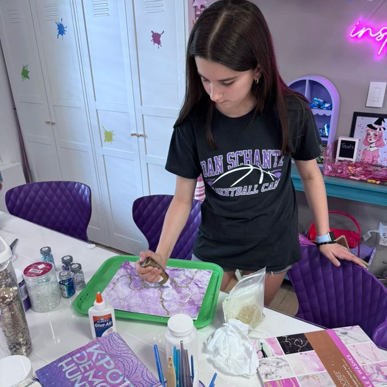 Young girl painting a craft project at a table in a room with colorful decor.