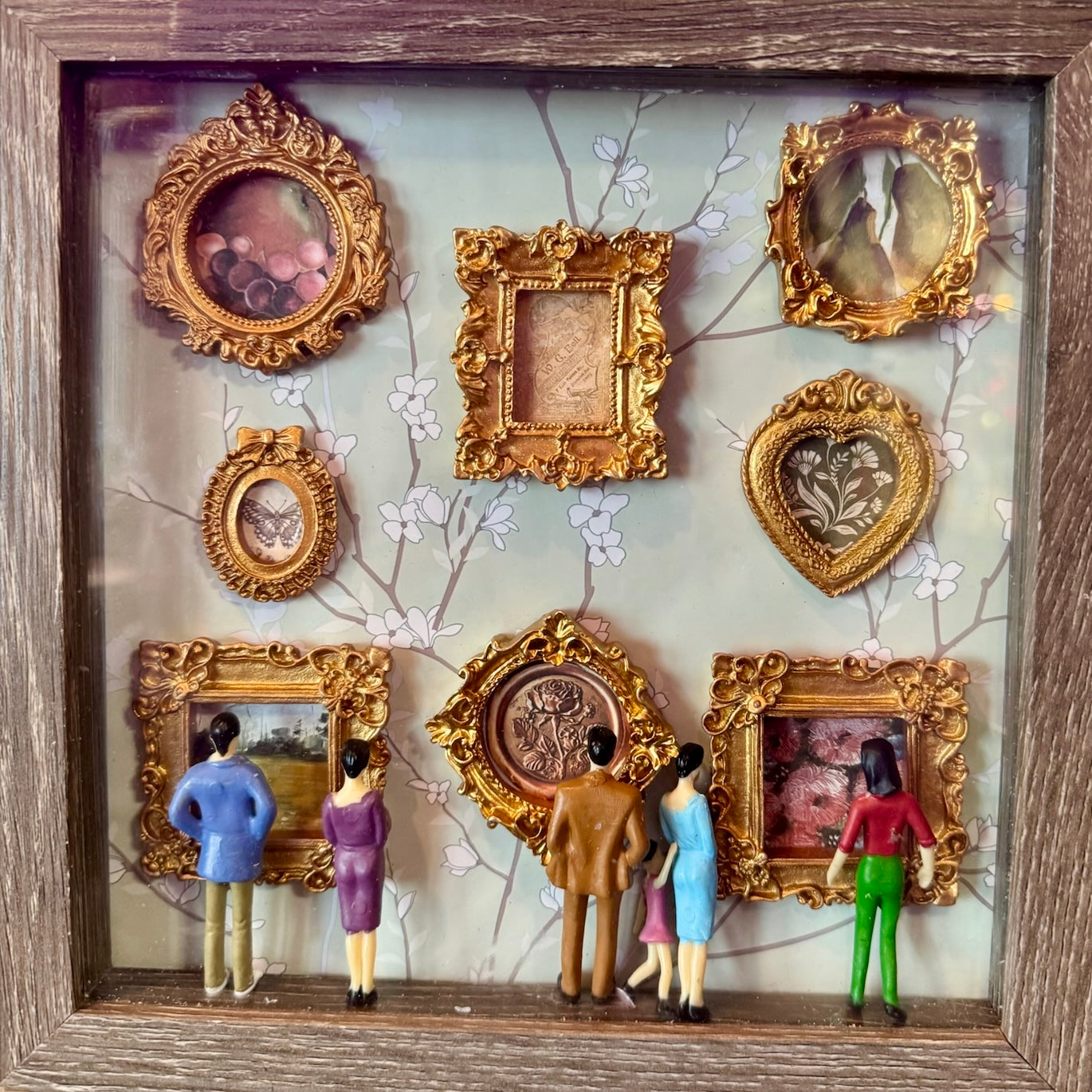 Decorative wall art with gold frames and small figures in a shadow box setting.