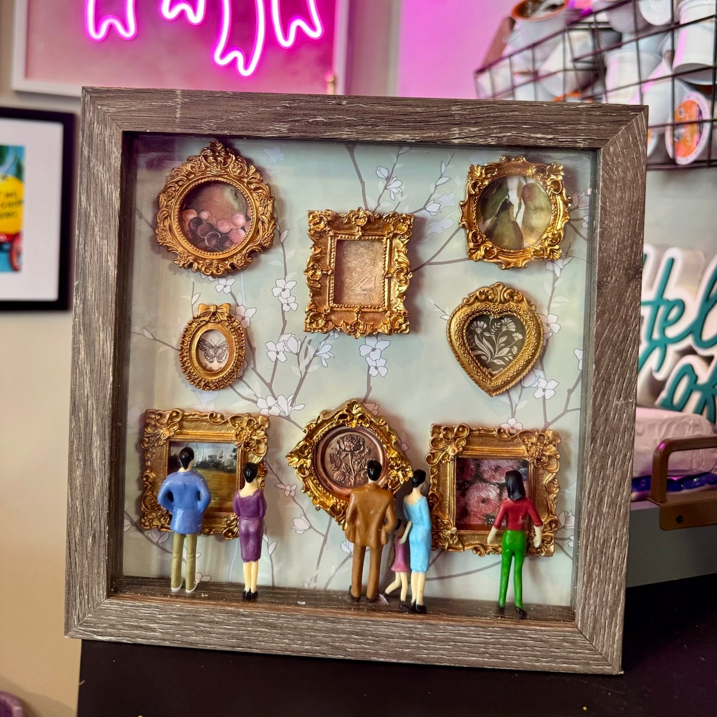 Decorative shadow box with gold frames and small figures in a room setting