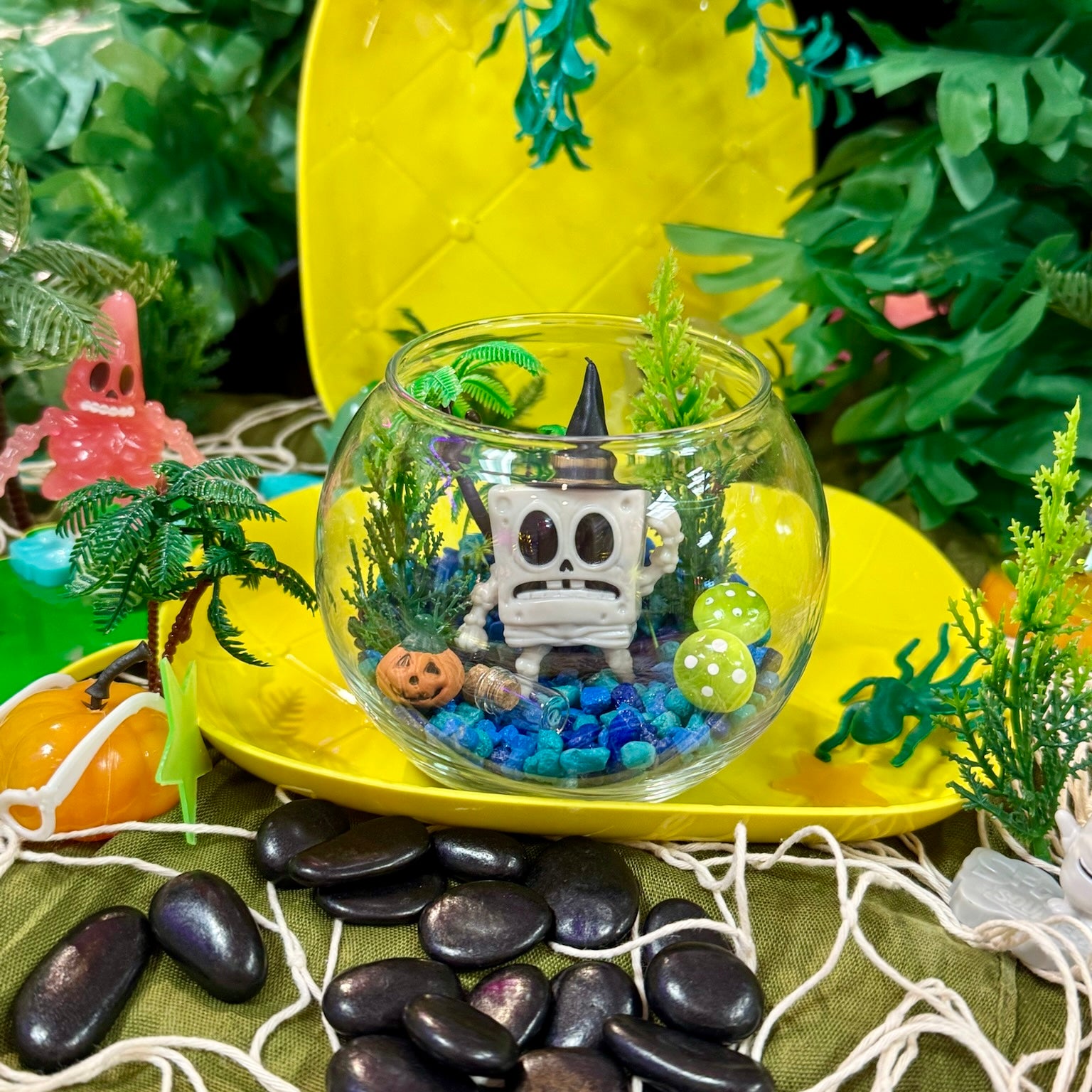 Small terrarium with a skeleton figure and plants on a yellow surface