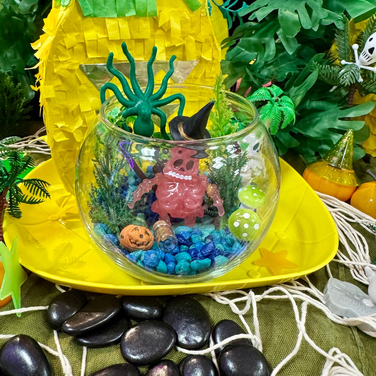 Glass bowl with Halloween-themed decorations on a yellow surface with greenery in the background