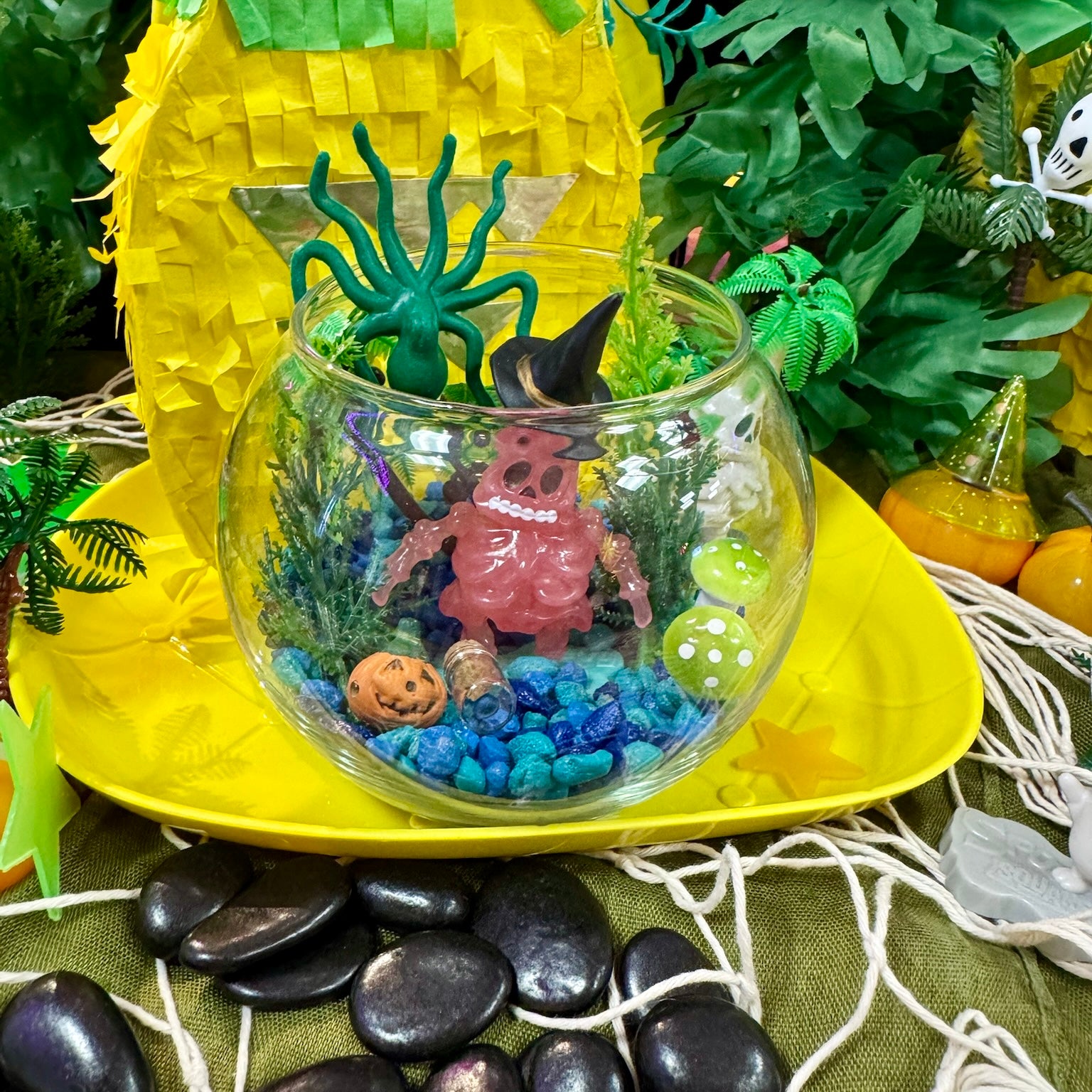 Glass bowl with Halloween-themed decorations on a yellow surface with greenery in the background