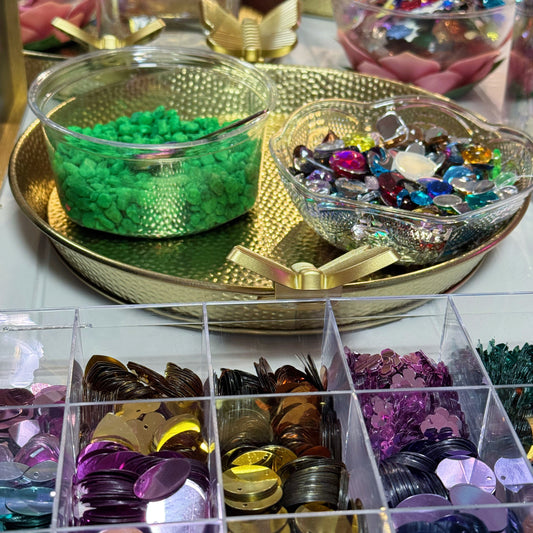 Assorted colorful beads and sequins in clear containers on a reflective surface.